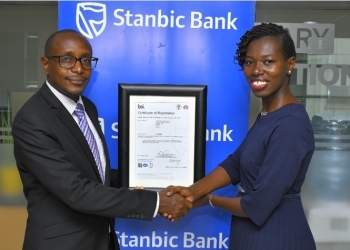 Louis Arinaitwe, Country Director, Department for International Trade and the Country Infrastructure and Trade Policy lead with the British High Commission, hands over ISO/IEC 27001:2013 Certification in recognition of its Information Security Management Systems (ISMS) compliance to global standards to Doreen Munanukye, Stanbic Bank's Ag Head of Information Security, at Umoja House today.