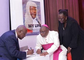Former Chief Justice Bart Katureebe autographs The Arch Bishop of Kampala Paul Semogerere as Former Vice President Specioza Kazibwe looks on.