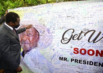 PPS Kenneth Omona reads through some of the messages on a banner wishing President Museveni a quick recovery before he received it to take to the president. The banner was placed at State House gate in Nakasero