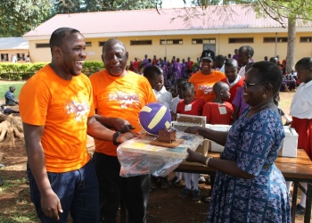The Head Teacher, Gulu Primary School, Lilly Rose Orem receives brail scholastic materials from Roke Telkom Account Relations Officer, while other staff and pupils look on