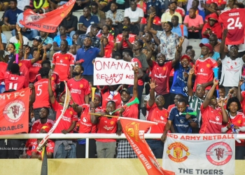 Manchester United fans in Uganda show their unwavering support for goalkeeper André Onana as they chant his name during the Cameroon vs Zimbabwe match at Namboole Stadium. The energetic crowd, clad in Manchester United jerseys and holding placards, demonstrates the club's massive following in the East African nation.