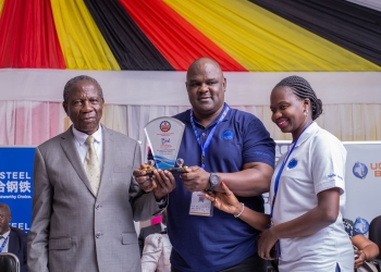 Hon. Matia Kasaija (in suit) handing over the Award to UCC's Joseph Kizito who was accompanied by a colleague at the official opening of the trade show last week.